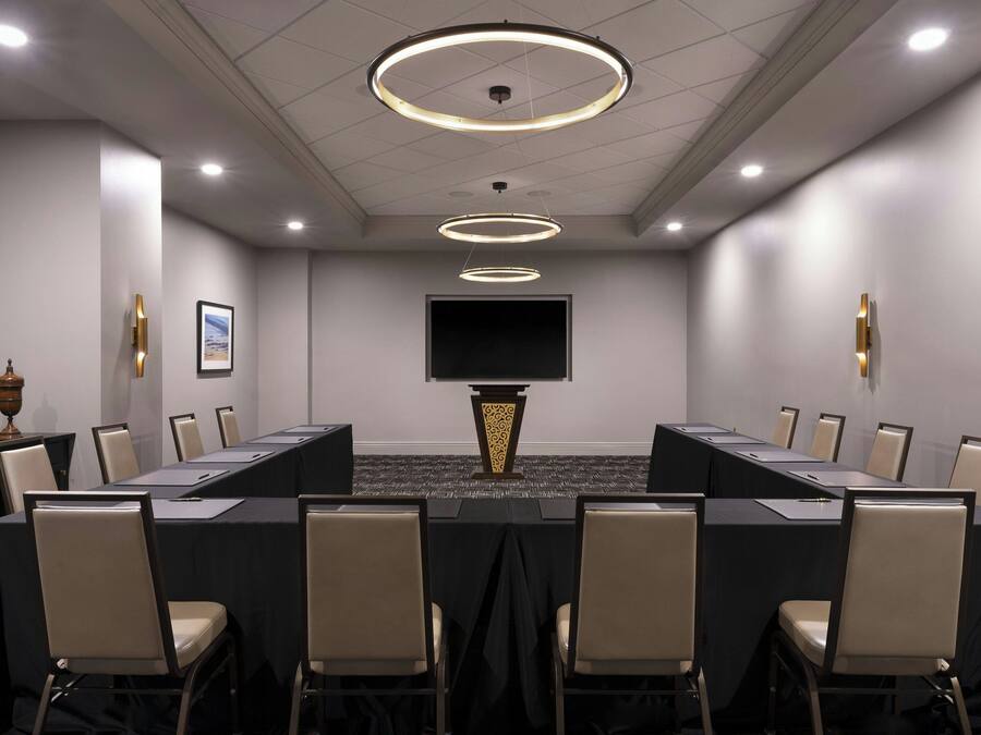 Una sala conferenze con un lungo tavolo, sedie, uno schermo televisivo e un vaso decorativo.