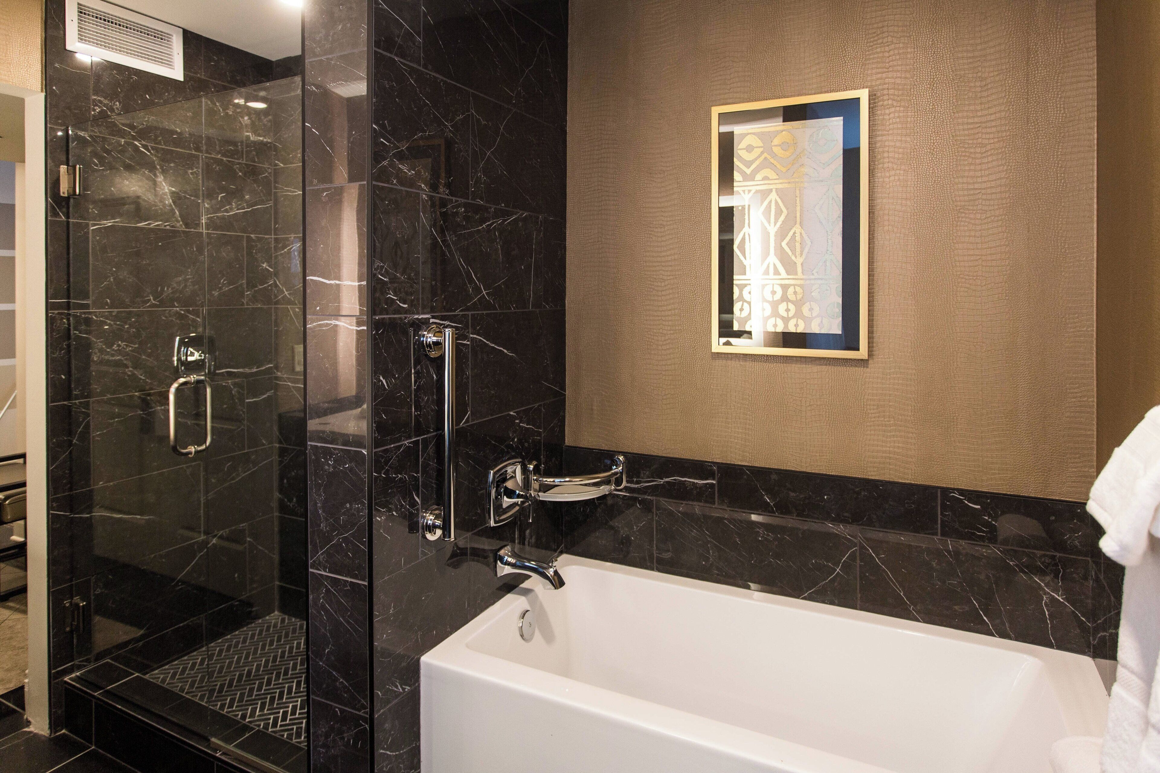 A modern bathroom with a glass-enclosed shower, a white bathtub, and a decorative wall piece.