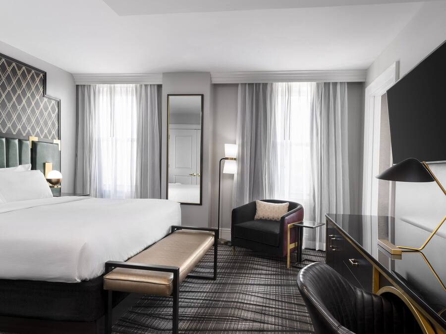 Una habitación de hotel con una cama grande, un escritorio con lámpara, una silla, un televisor y un espejo.