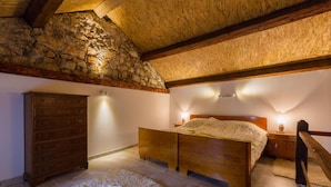 A bedroom with a stone wall, wooden bed, dresser, and a fluffy rug. - Villa Holiday Coral (Vinodol)