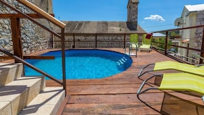 A pool area with a stone wall, wooden deck, and lounge chairs. - Villa Holiday Coral (Vinodol)