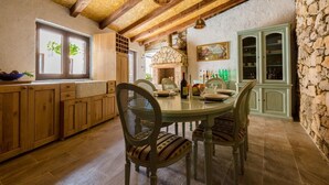 A rustic kitchen with wooden cabinets, a stone wall, and a dining table with chairs. - Villa Holiday Coral (Vinodol)