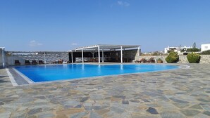 Una piscina con cubierta de baldosas de piedra, una zona de estar techada y vistas al paisaje circundante.