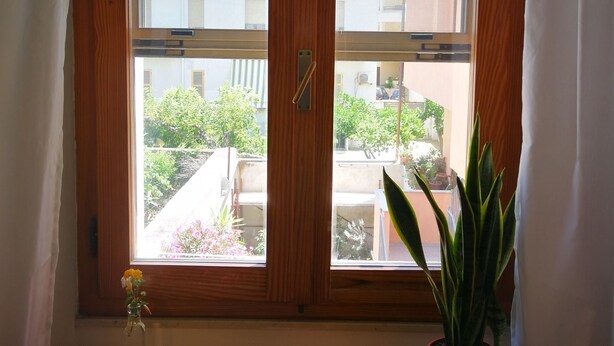 Una ventana con vistas a un balcón y una planta en maceta sobre una mesa de madera.