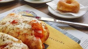 Una mesa con un croissant, una taza de café, un donut y un plato con un pastel horneado.