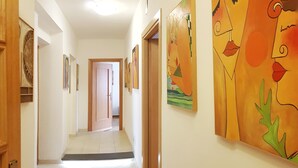 Un pasillo con suelo de baldosas, puertas de madera y varias obras de arte en las paredes.