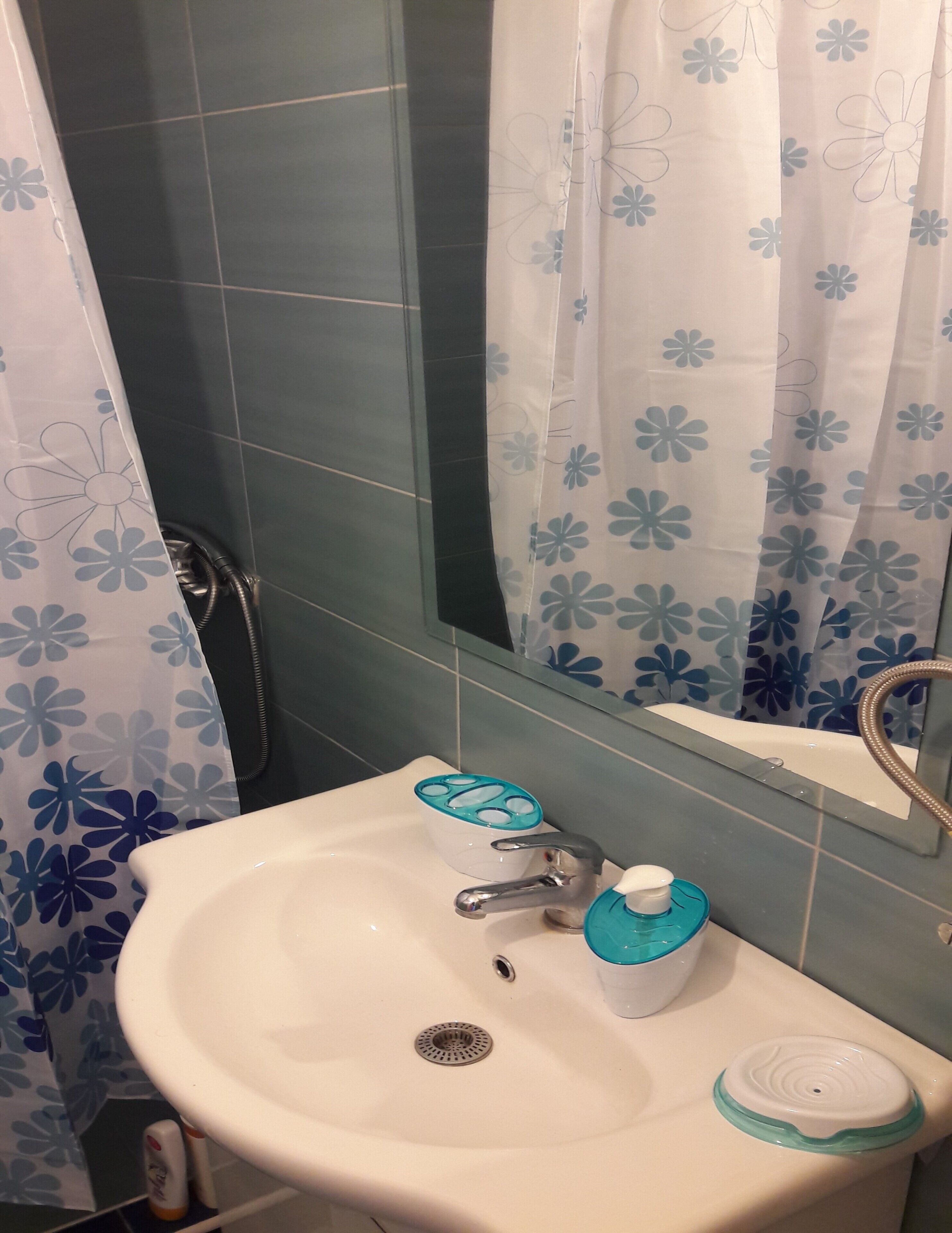 Ein Badezimmer mit Waschbecken, Spiegel, einer Duschkabine mit Blumenmuster und einer Duschbrause.