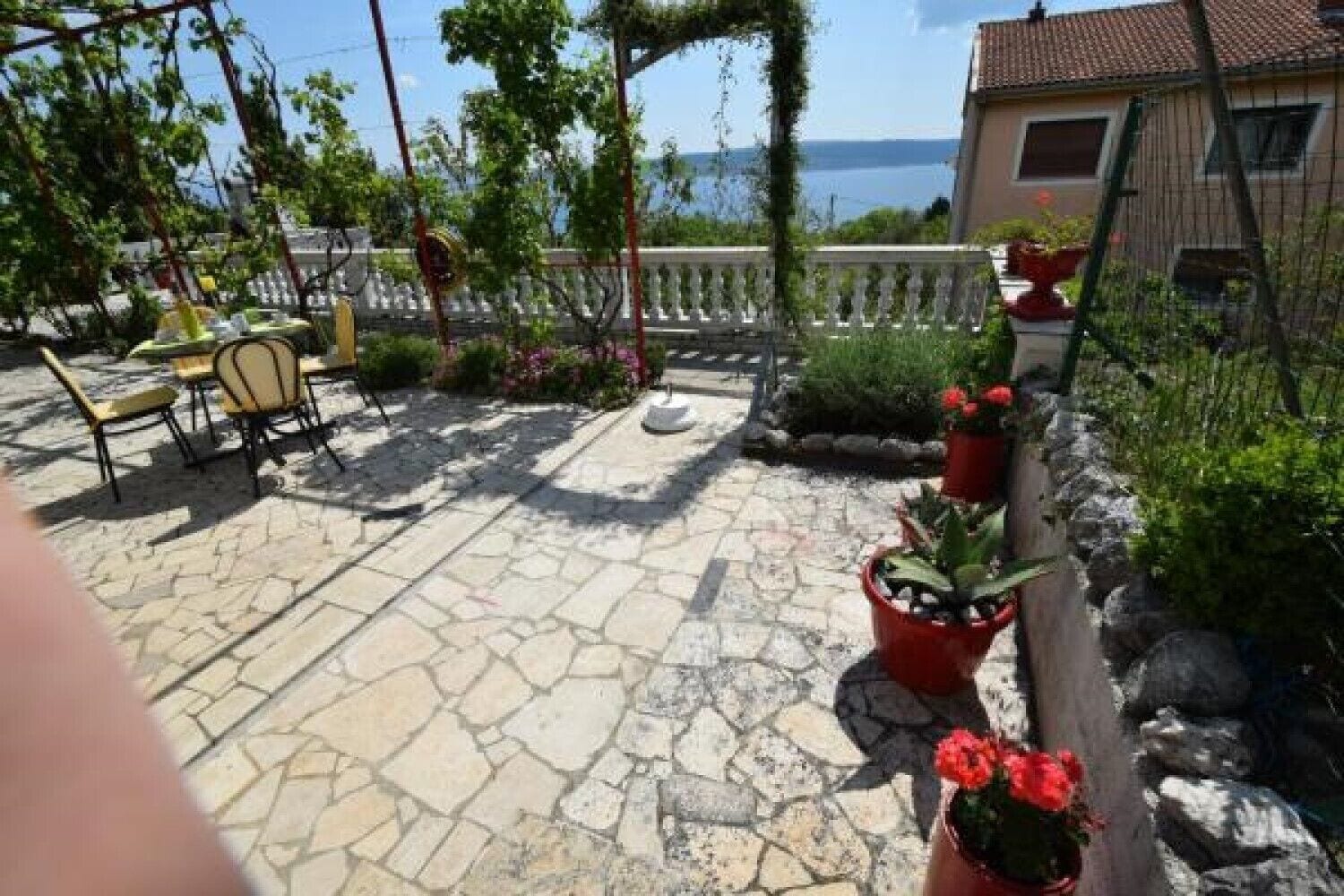Une terrasse avec un sol en pierre, des meubles d’extérieur, des plantes en pot et une vue sur la mer.
