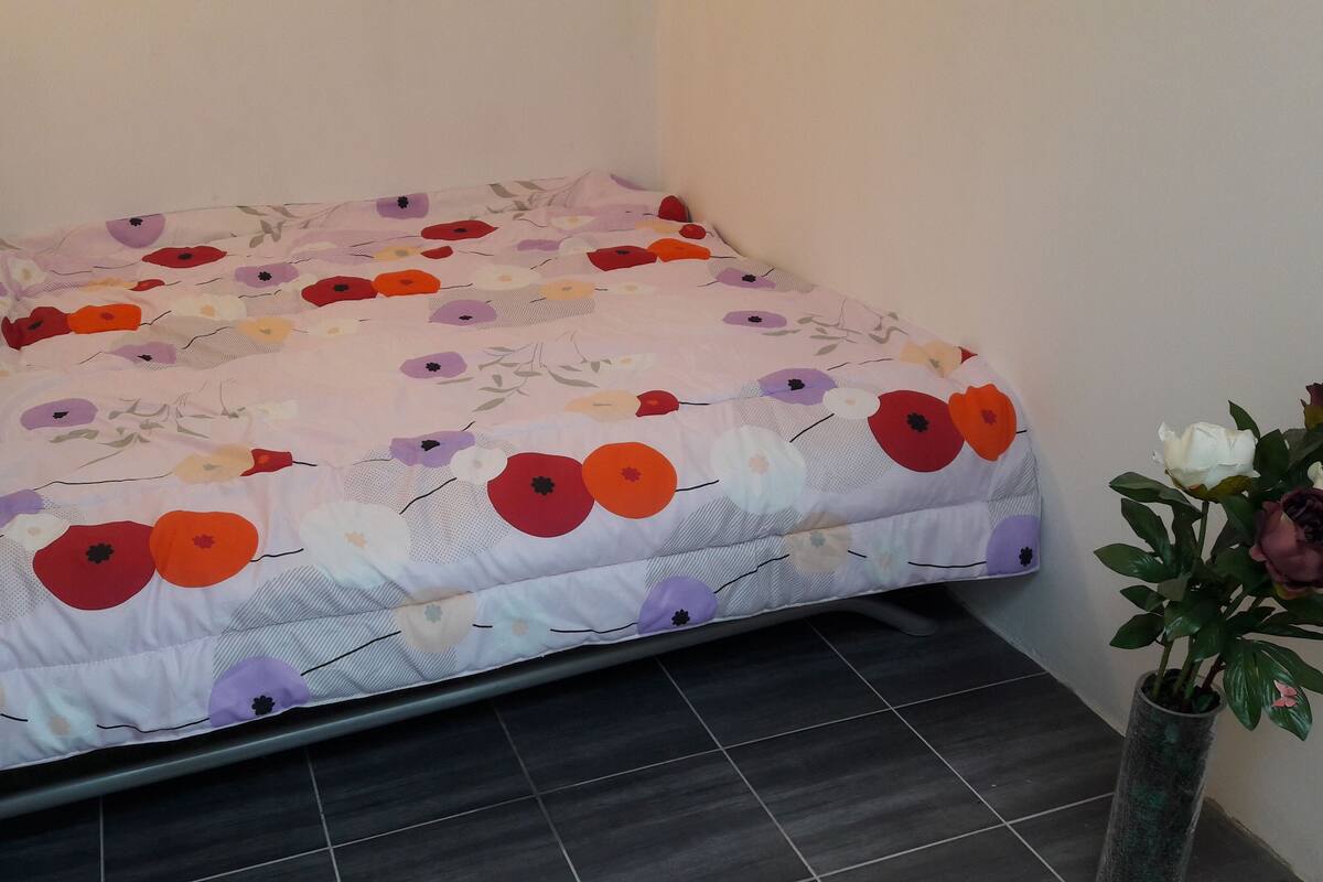 A bed with a floral bedspread in a room with dark tiled flooring and a potted plant.