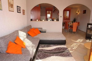 A living room with a sofa, a rug, and a dining area visible through an archway.