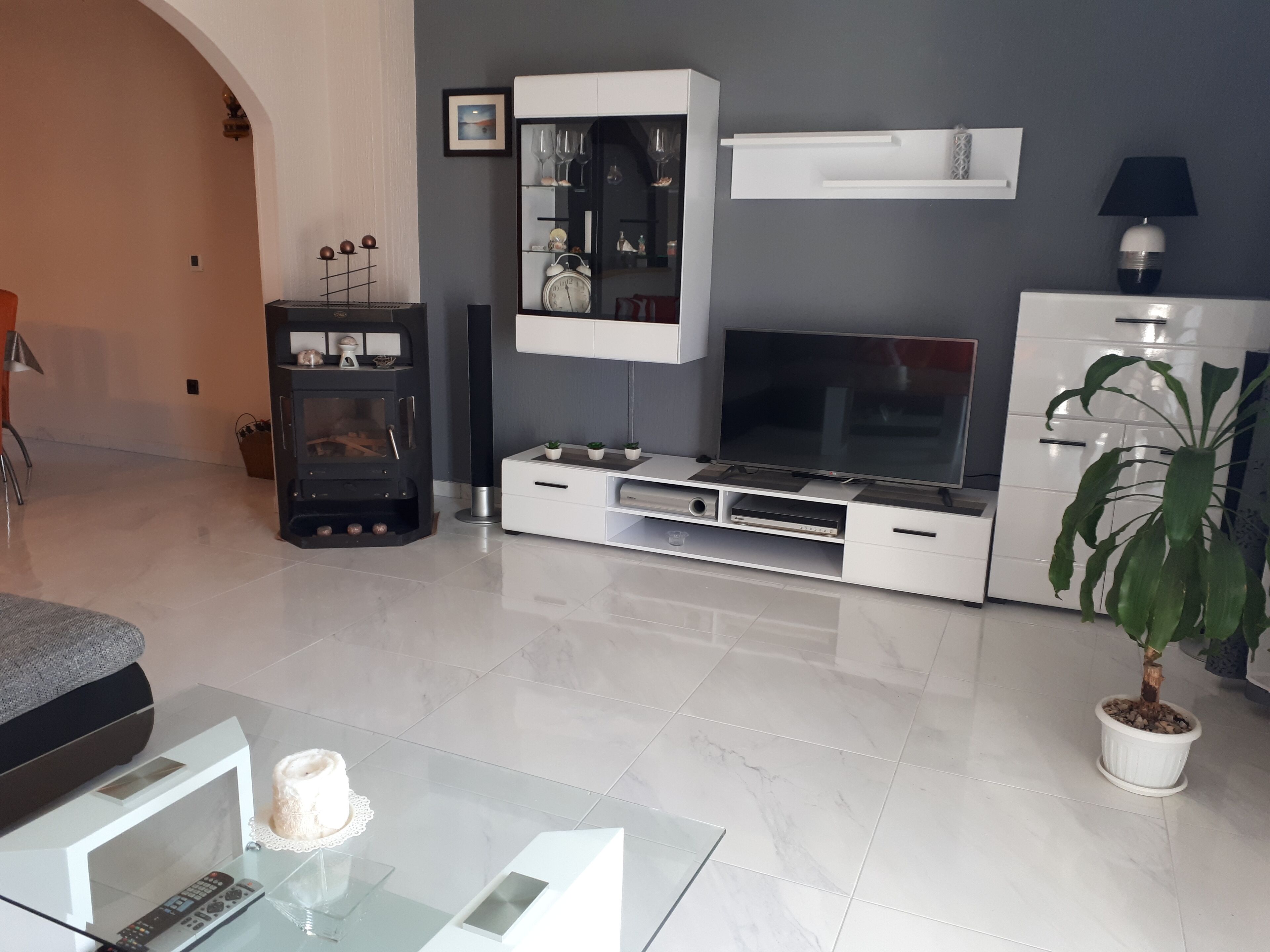 A modern living room with a flat-screen TV, white cabinetry, a glass coffee table, and a potted plant.