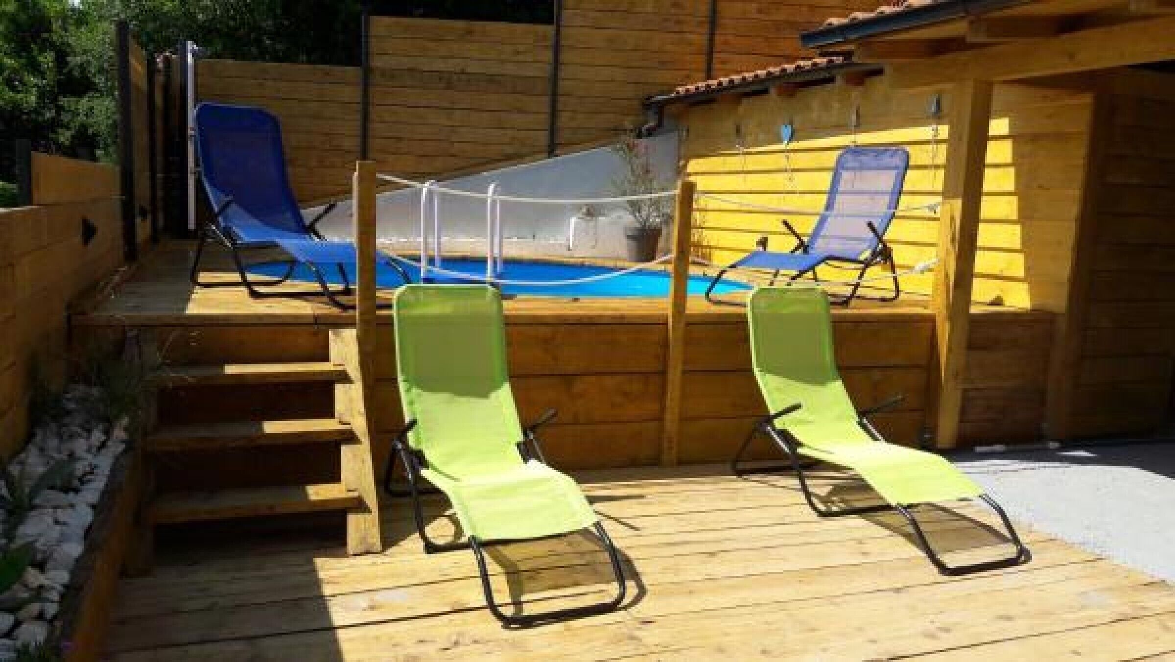 Um deck de madeira com duas espreguiçadeiras verdes e uma pequena área de piscina.