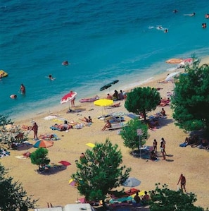A beach with people swimming and sunbathing, umbrellas, and beach chairs. - Apartments Jasminka (Crikvenica)