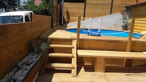 A wooden deck with a pool, steps, and a fenced area.