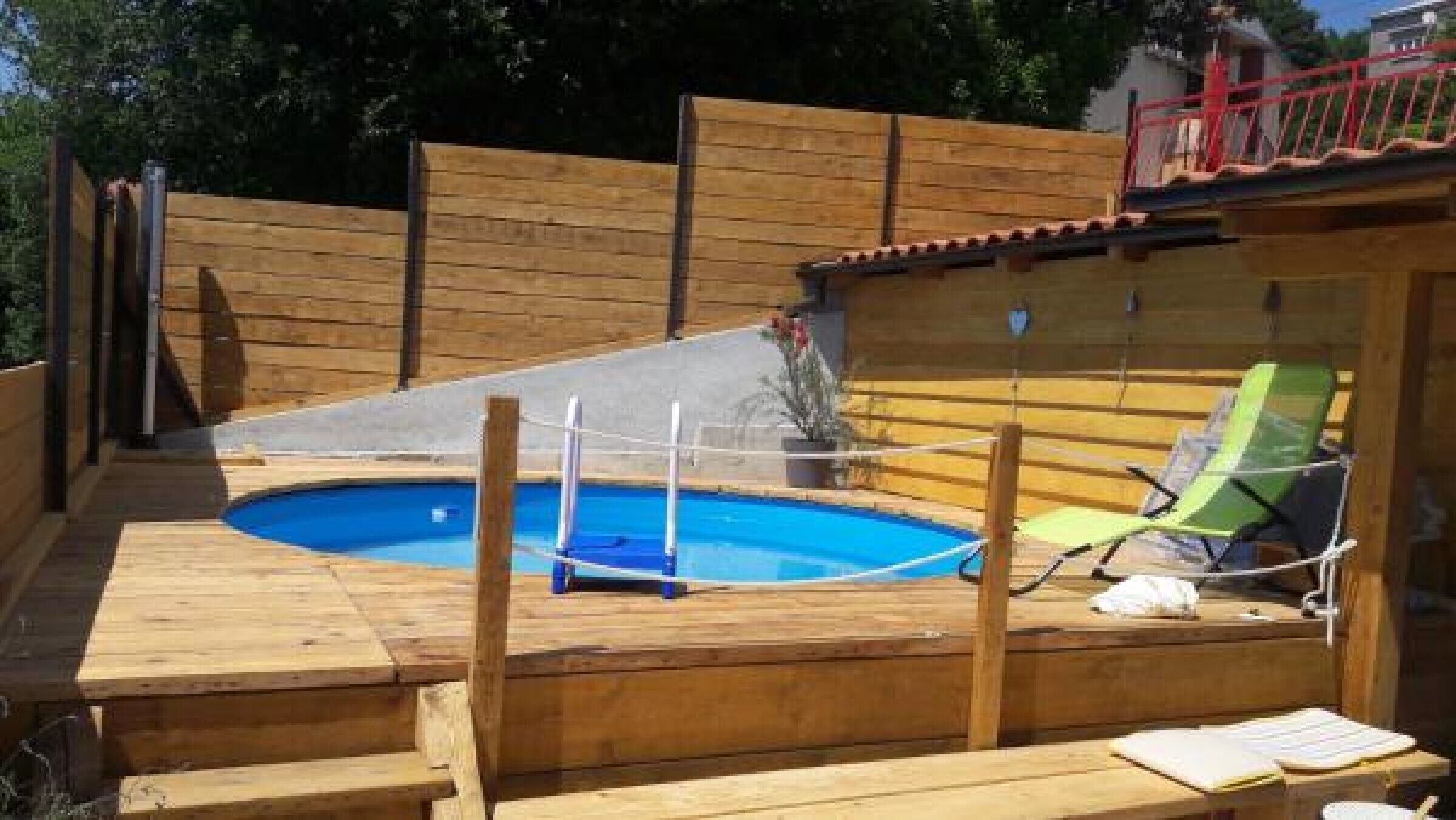 Eine Holzterrasse mit Swimmingpool, einer kleinen Rutsche und einem grünen Liegestuhl.
