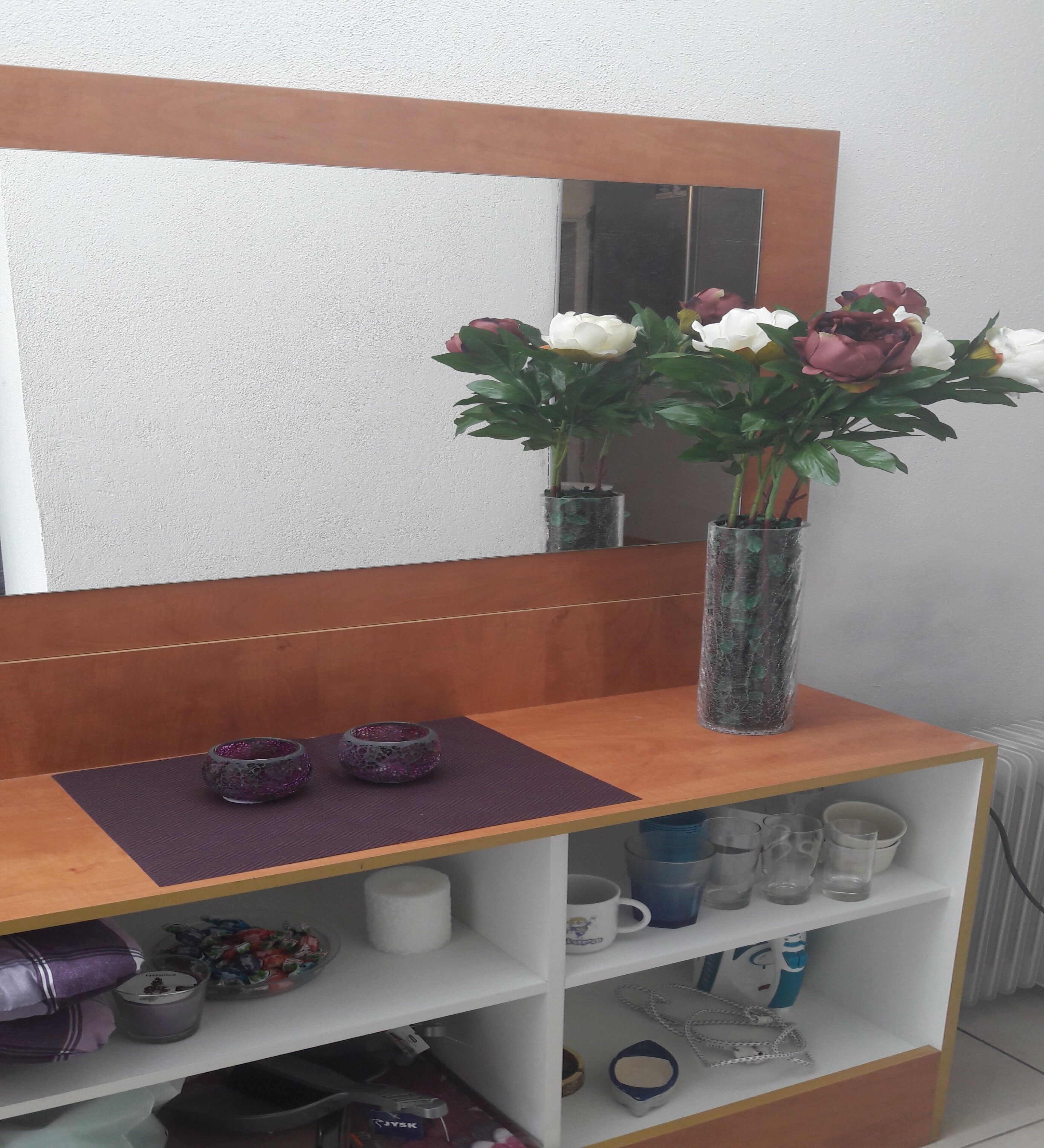 A wooden shelf with a vase of flowers, a purple mat, and decorative bowls.