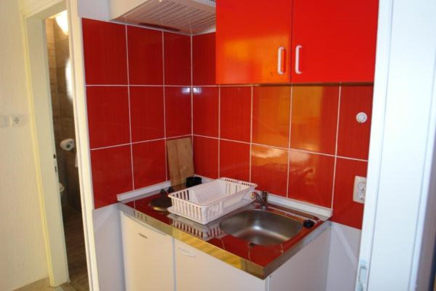A compact kitchen with red tiles, a white countertop, and a small sink.