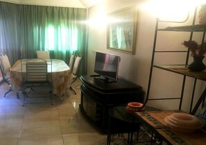 A living room with a dining table, chairs, a TV, a sofa, and a TV stand. - Pool View Apartment in the Center of Marrakech 4571 (Marrakech)