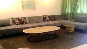 Uma sala de estar com um sofá cinza, uma mesa de centro redonda e uma mesinha lateral.