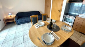 Un coin repas avec une table ronde en bois, dressée pour quatre personnes, un canapé bleu et une cuisine dotée de meubles en bois et d’une cuisinière.