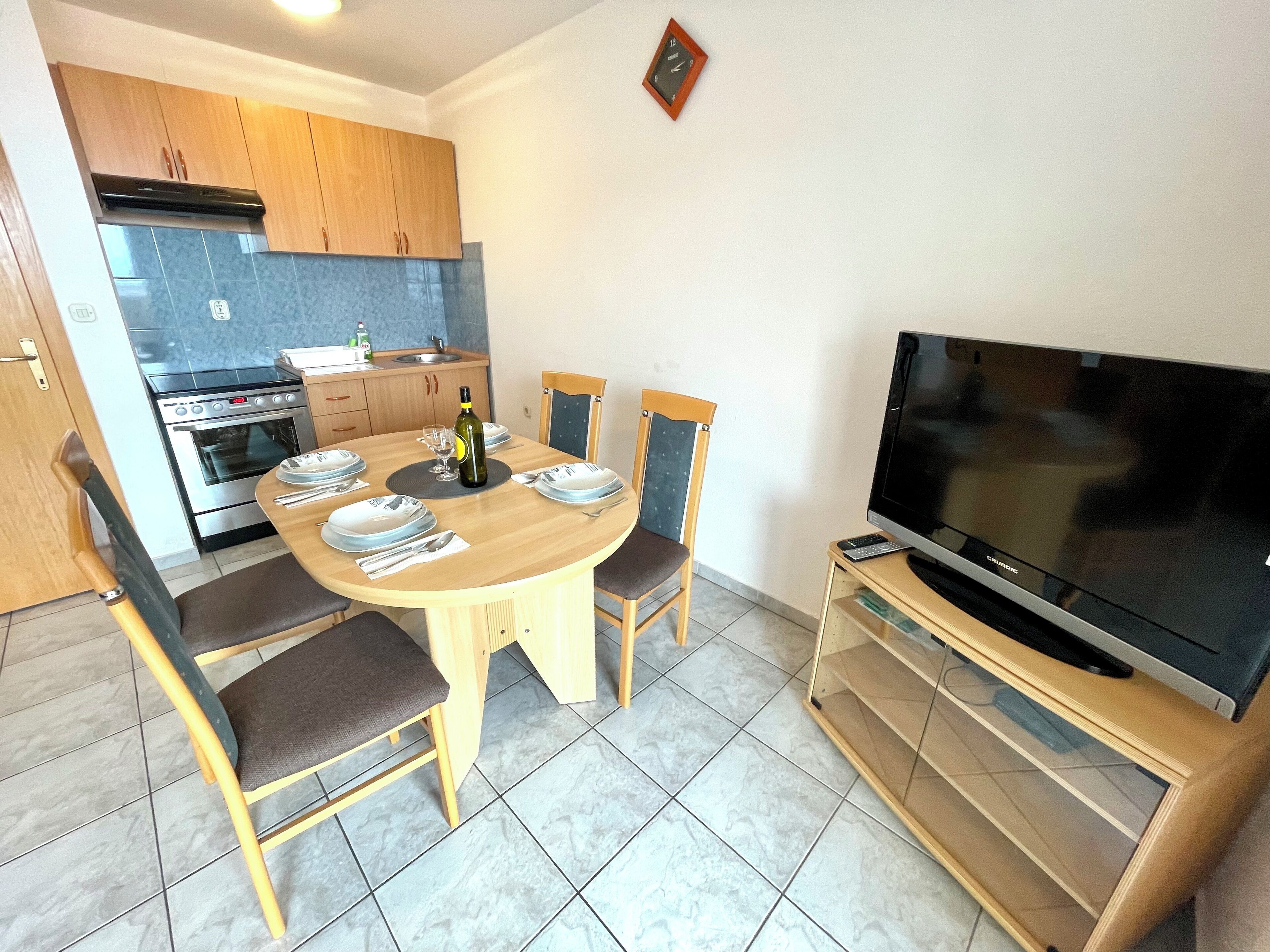 A compact kitchen with modern appliances, a dining area with a round table and chairs, and a TV on a stand.