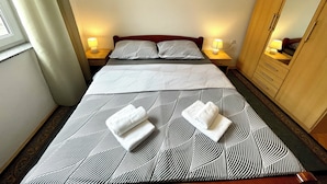 Un lit double avec une couvre-lit à motifs géométriques, deux oreillers, deux lampes de chevet, une armoire en bois et deux serviettes pliées posées sur le lit.