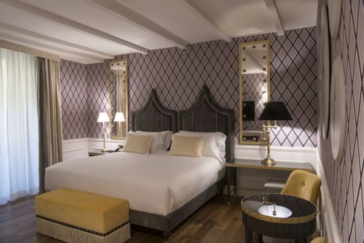 Habitación de hotel con una cama grande, mesitas de noche, una silla y una pequeña mesa con lámpara.