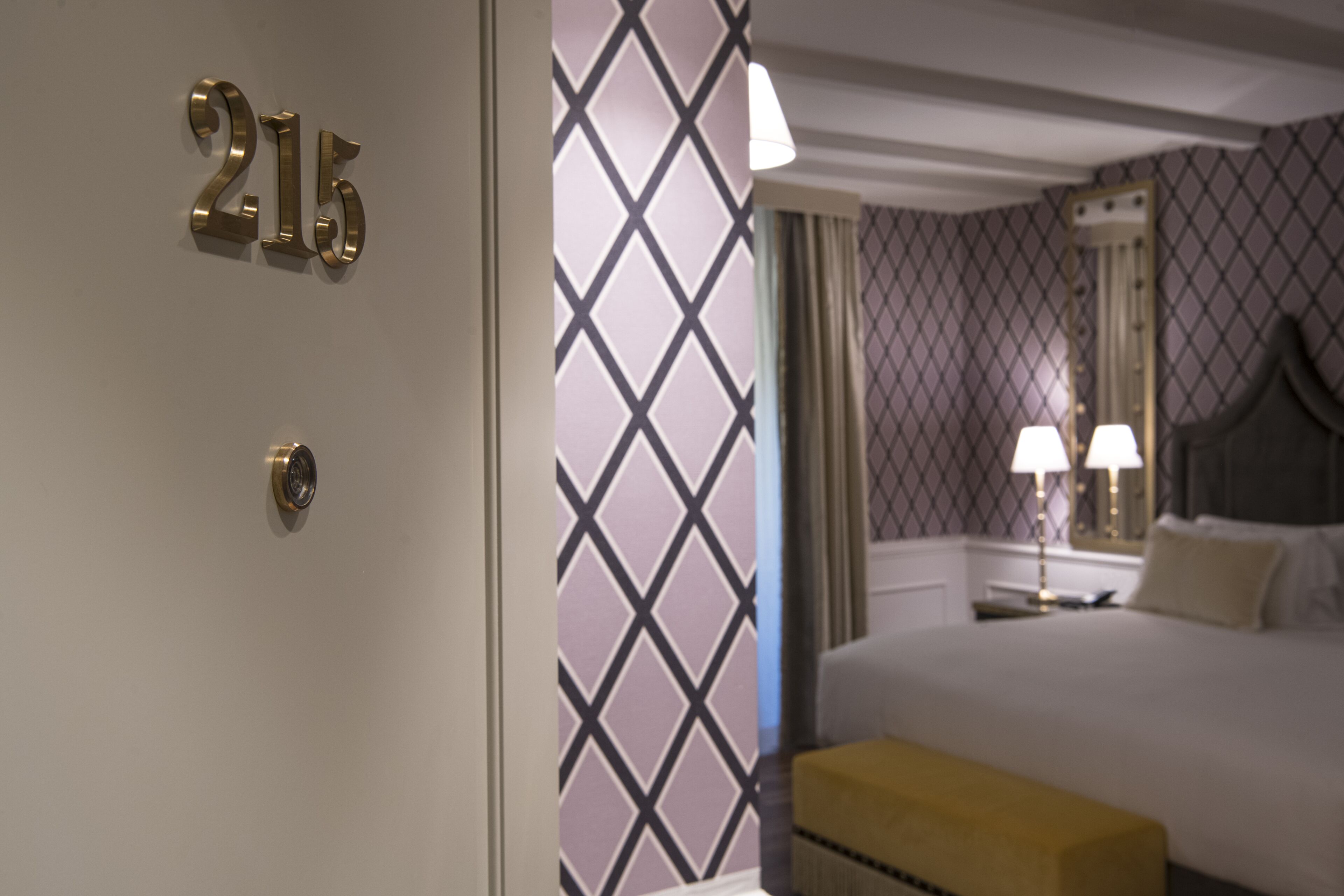 Una camera d'hotel con un letto, un comodino, una lampada e una parete con motivo geometrico.