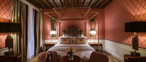 Habitación de hotel con una cama grande, dos mesitas de noche, una mesa redonda con un jarrón de flores y dos sillones.