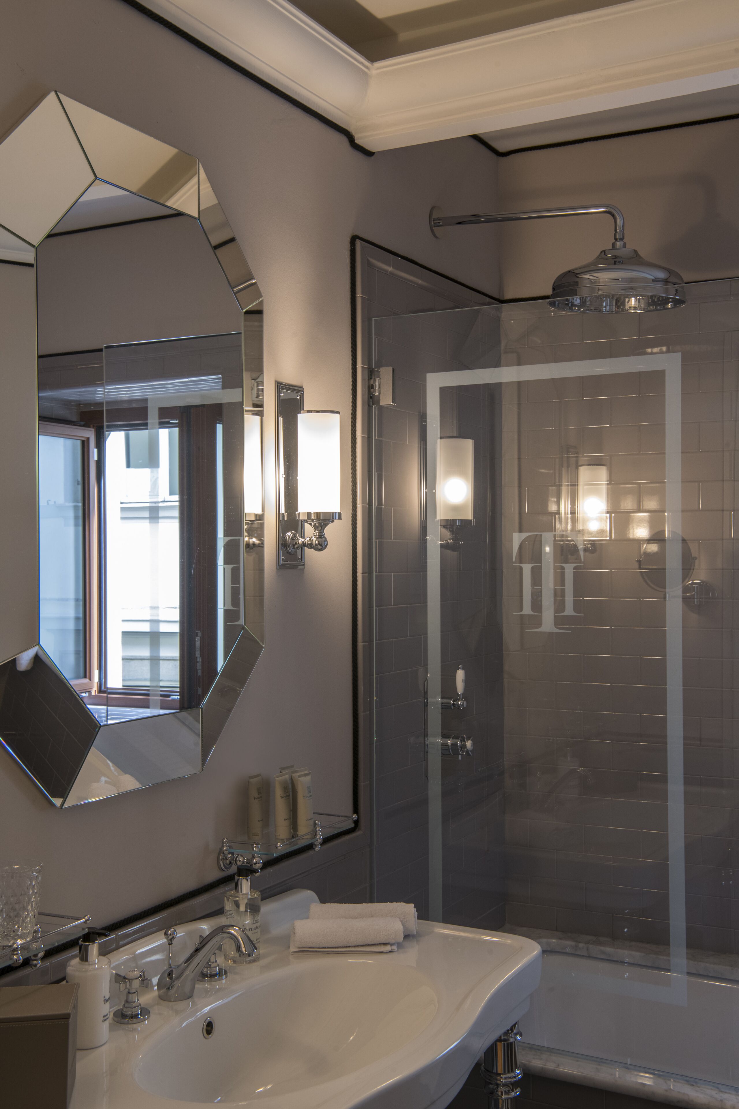 Une salle de bain moderne avec un grand miroir, un lavabo, une douche et un espace douche fermé par des parois de verre.