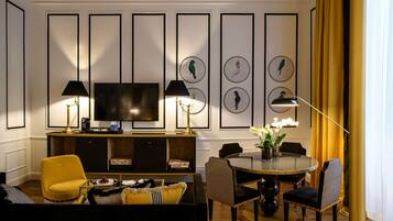 A modern living room with a flat-screen TV, two lamps, a yellow armchair, a dining table with chairs, and framed wall art.
