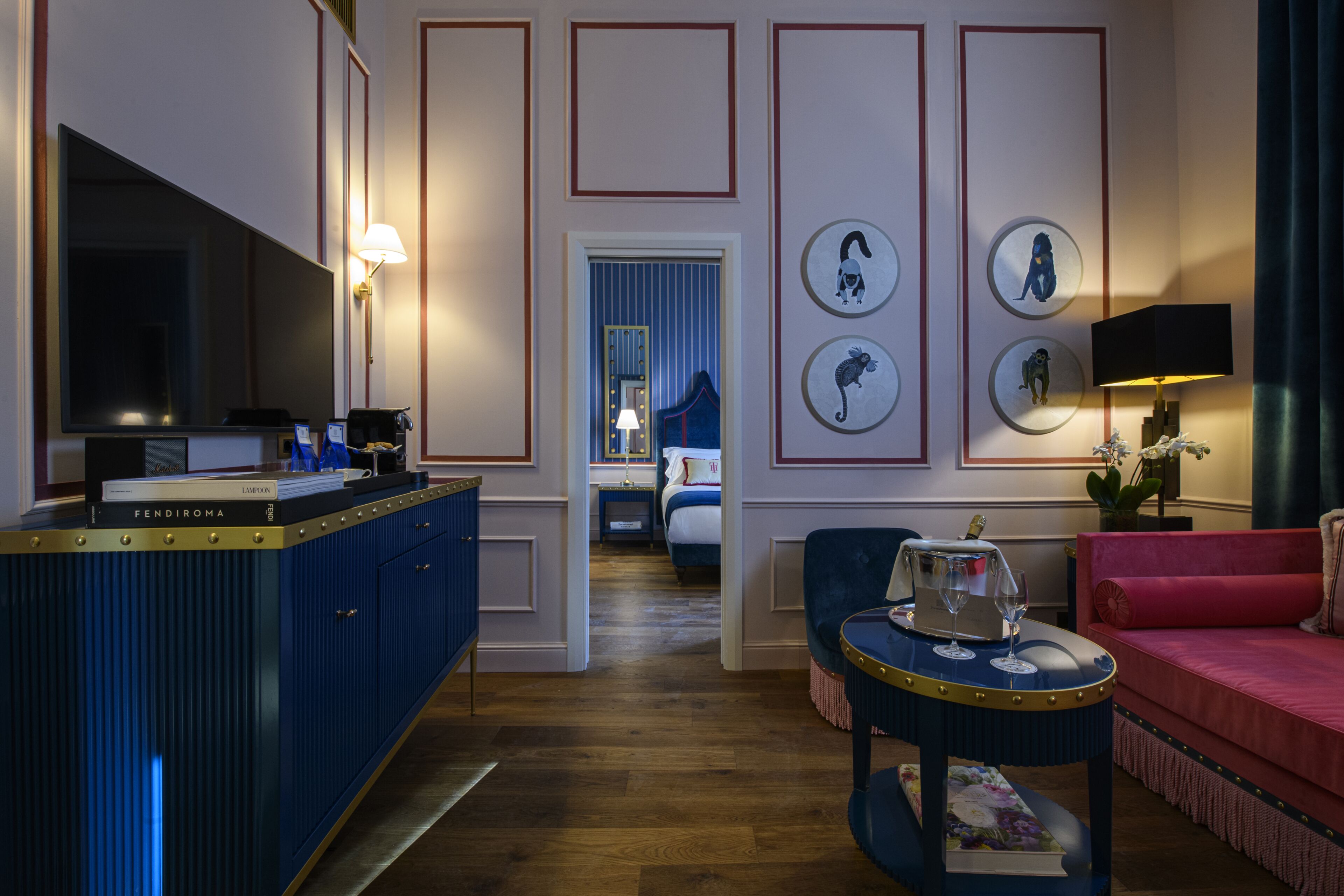 Une chambre d’hôtel avec un mini-bar bleu, un canapé rouge, une table basse ronde et un lit avec une tête de lit bleue.
