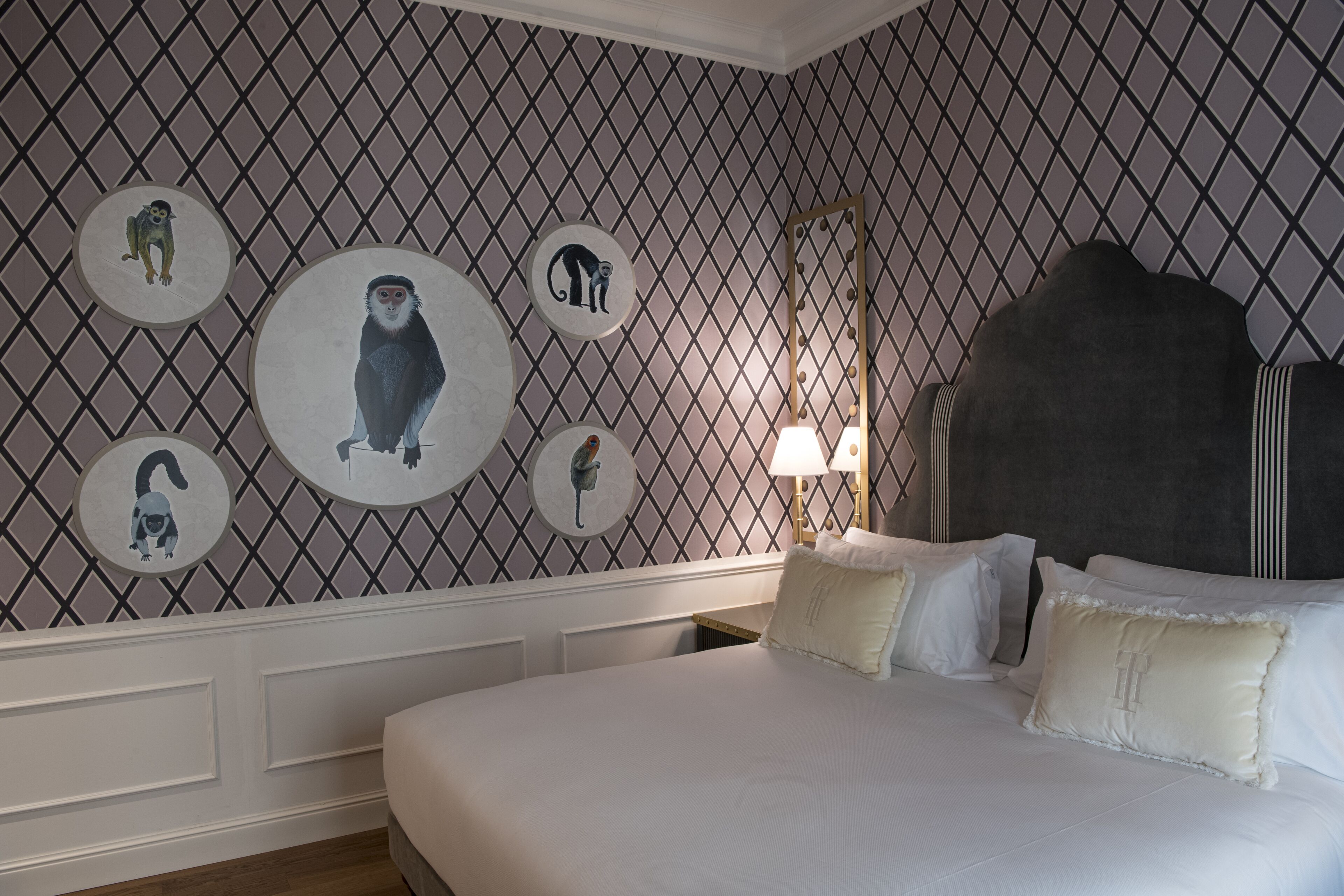Habitación de hotel con una cama grande, cabecero, pared decorada con estampados de animales circulares y mesita de noche con lámpara.
