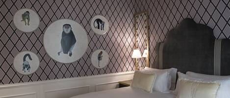 Habitación de hotel con una cama grande, cabecero, pared decorada con estampados de animales circulares y mesita de noche con lámpara.