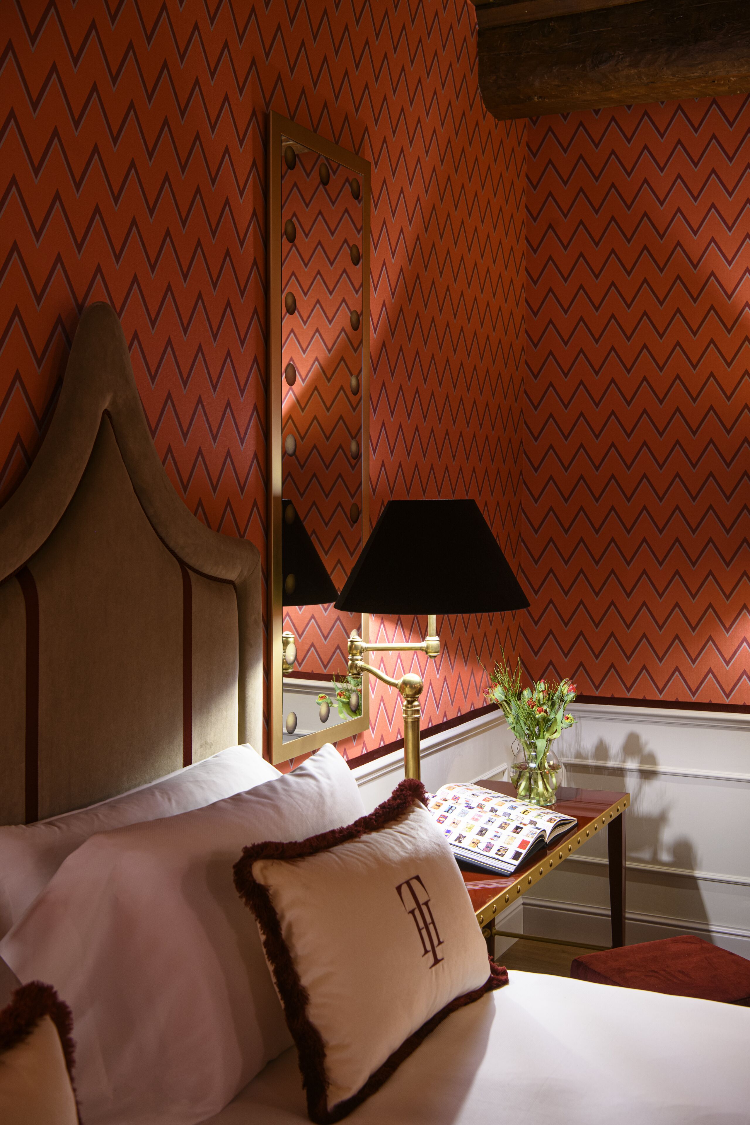 A hotel room with a bed, a bedside table with a lamp, and a mirror on the wall.