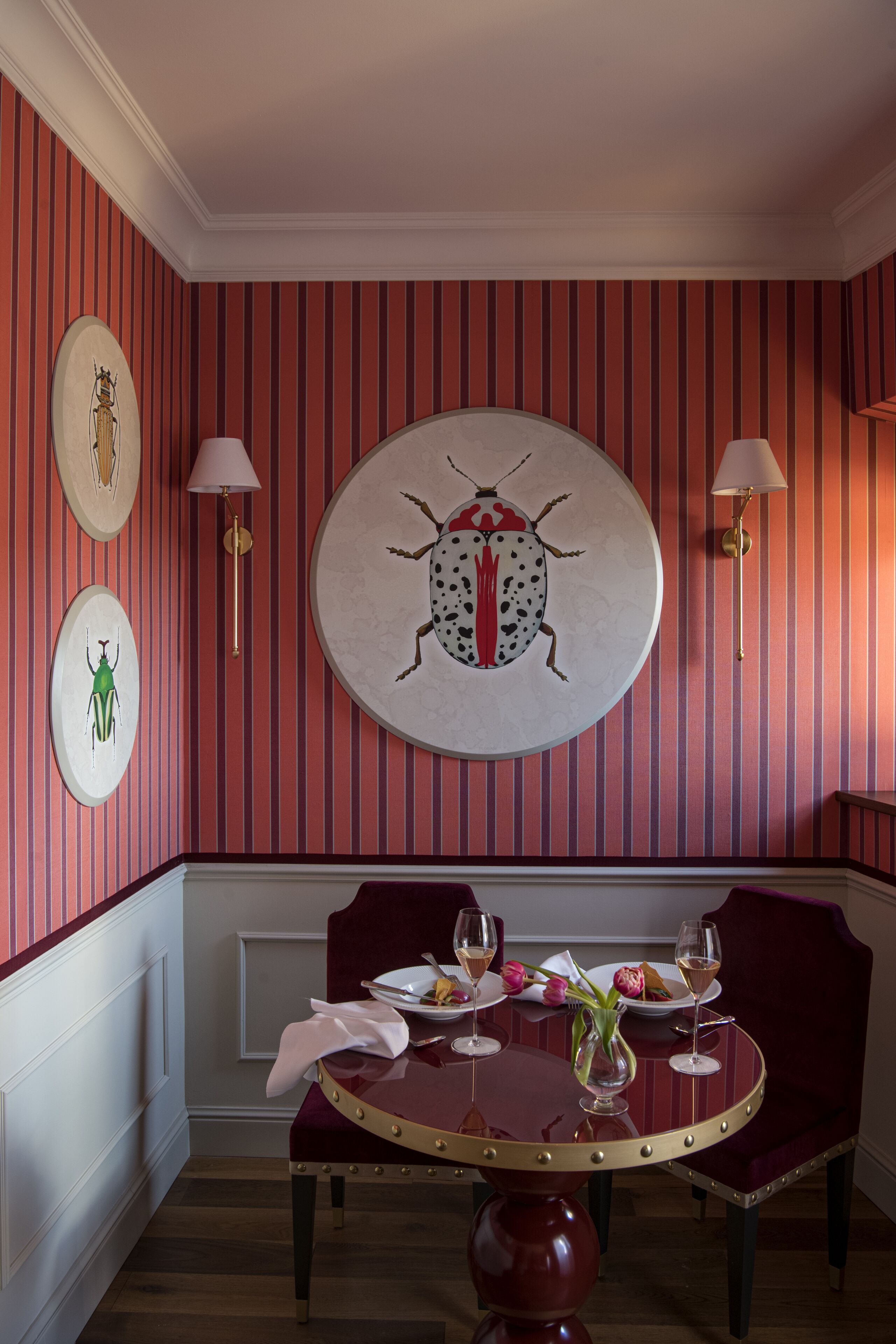Zona pranzo con tavolo rotondo, sedie imbottite rosse e un'opera d'arte circolare a parete.