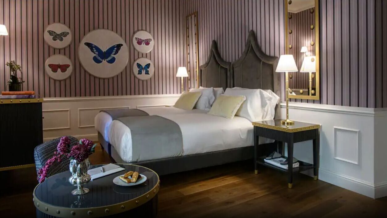 A hotel room with a bed, bedside table, lamp, and decorative butterfly wall art.