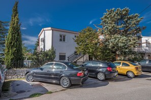 A row of parked cars in front of a building with a white facade and a staircase leading to an upper level. - Apartment Miky (Crikvenica)