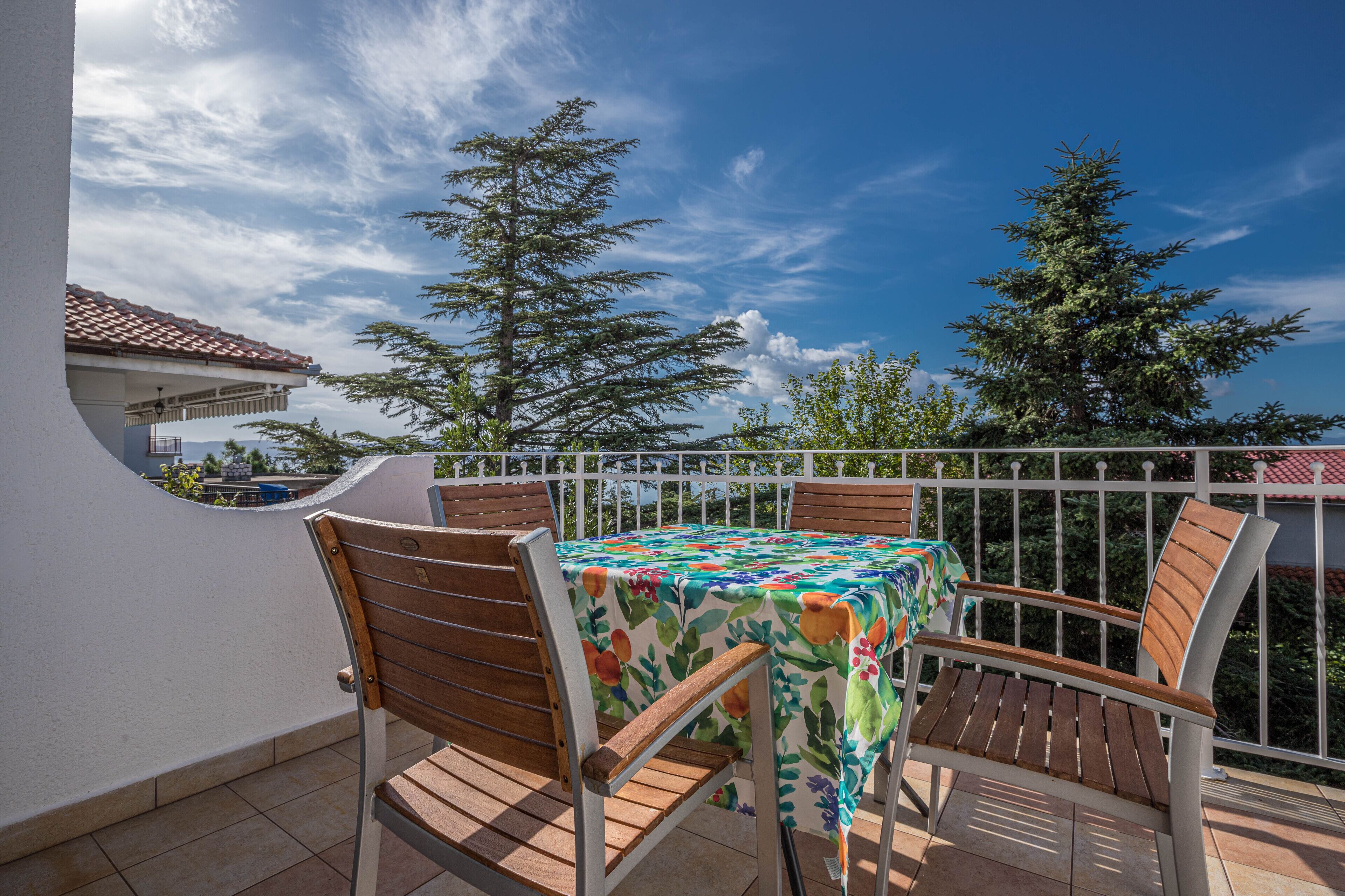 Un balcon avec une table et des chaises, une balustrade et des arbres en arrière-plan.