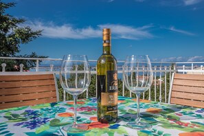 A table with a floral tablecloth, a bottle of wine, and two glasses on a balcony with a view of the sea. - Apartment Miky (Crikvenica)
