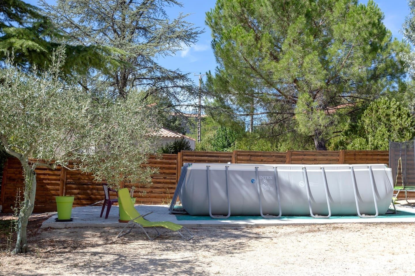 An outdoor swimming pool area with a covered pool, a wooden fence, and a tree.