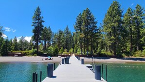 A wooden pier extending into a clear blue lake, surrounded by dense green trees.