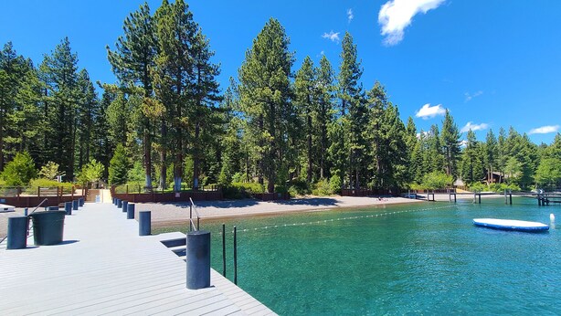 A wooden dock extending into a clear blue pool surrounded by tall trees.