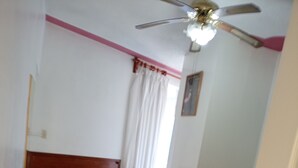A bedroom with two beds, a ceiling fan, a window with curtains, and a door. - Posada Reforma (Oaxaca)