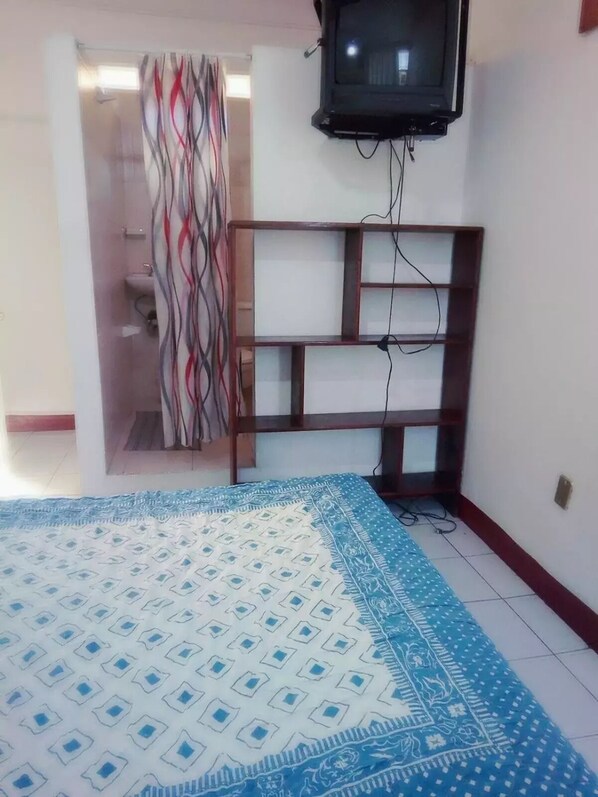 Une chambre à coucher avec un lit, un téléviseur fixé au mur, une armoire et un tapis à motifs.