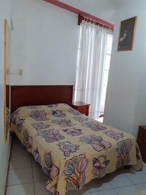 Une chambre à coucher avec un lit, une tête de lit en bois, une table de chevet, une fenêtre avec des rideaux blancs et un tableau accroché au mur.