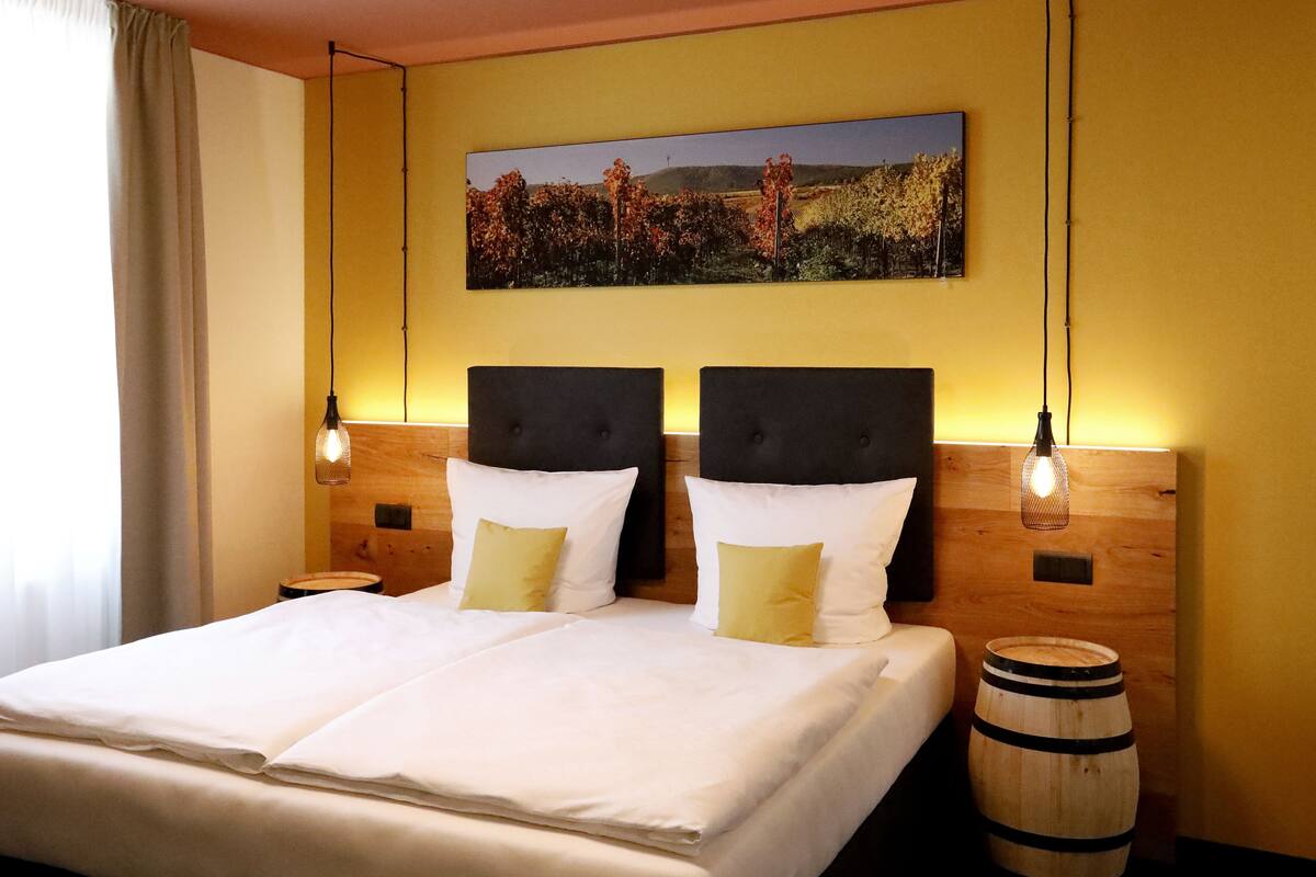 Una cama doble con almohadas blancas y amarillas, un cabecero de madera y un barril de madera a su lado.