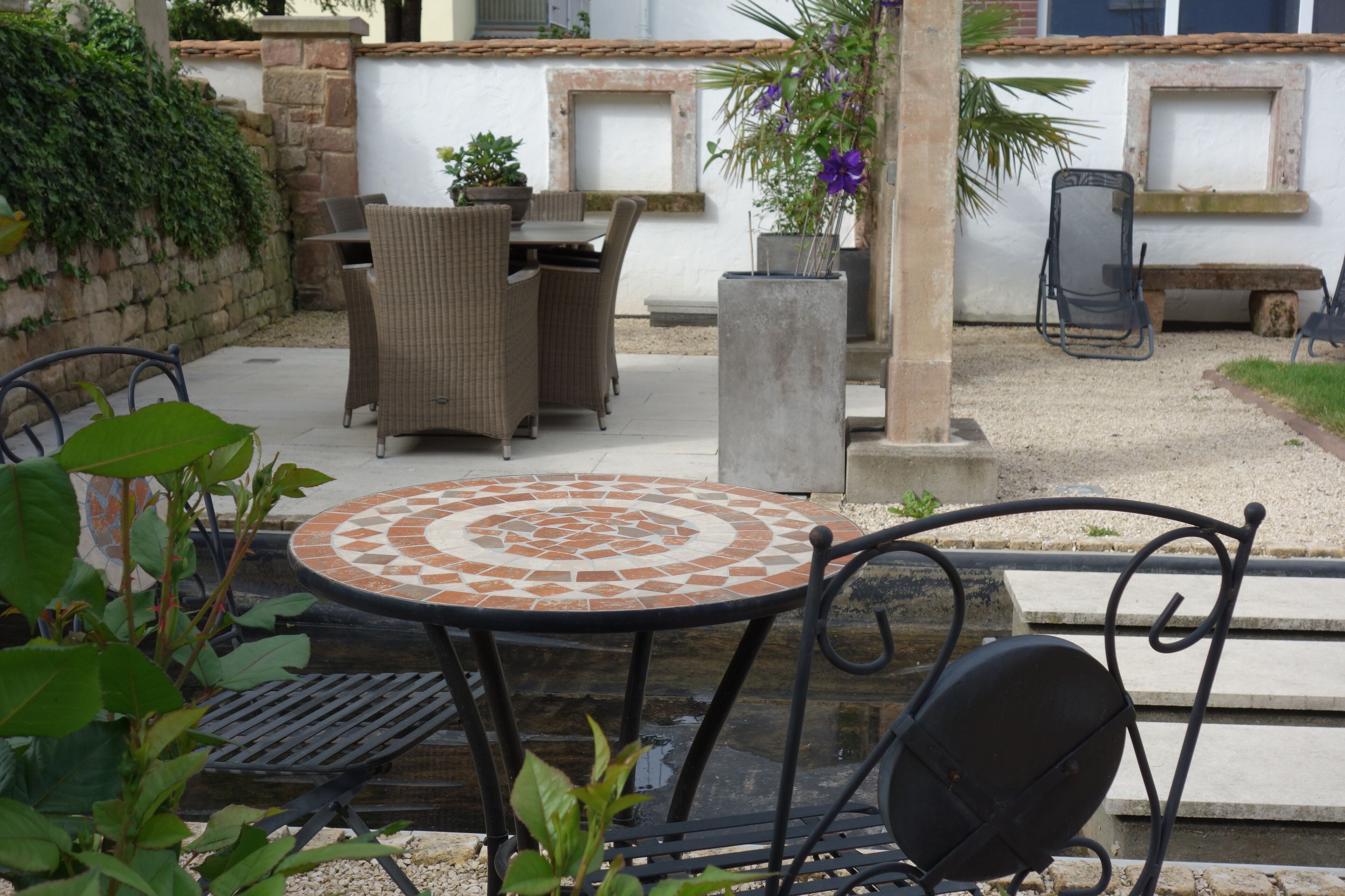 An outdoor patio with wicker furniture, a tiled table, and potted plants.