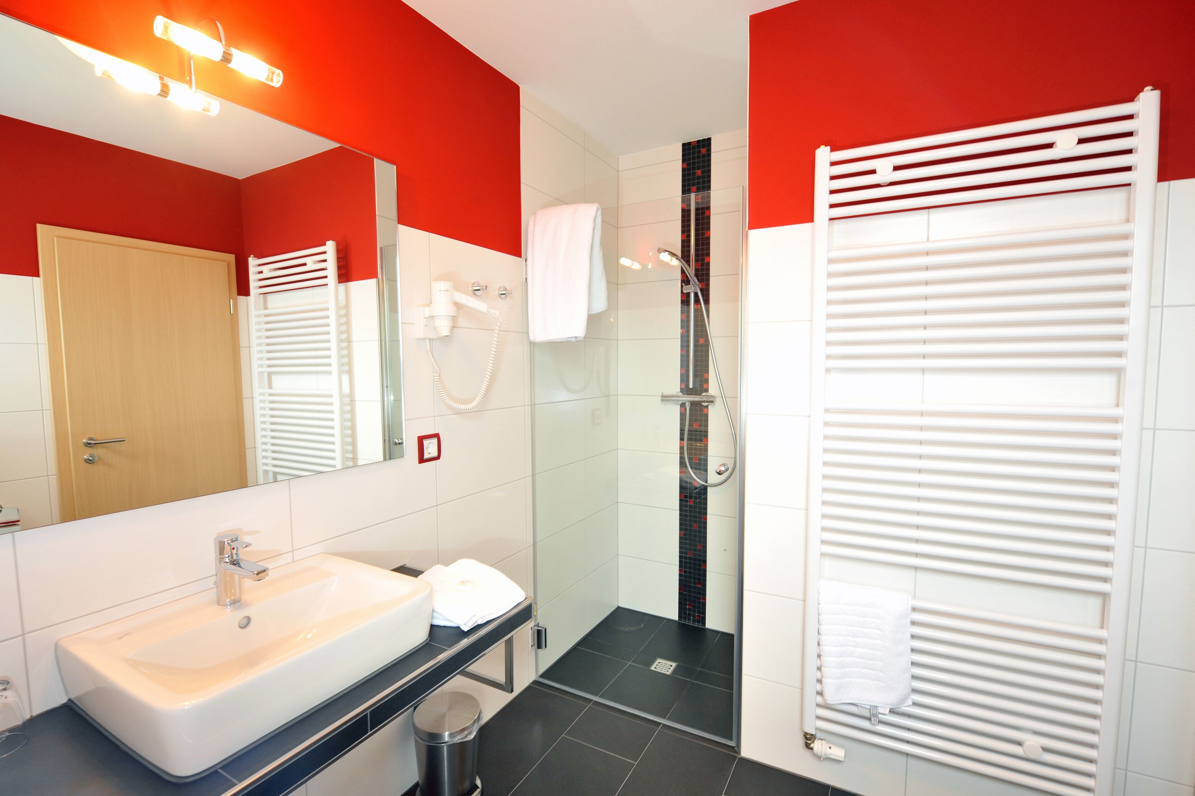 A modern bathroom with a large mirror, white sink, and a glass-enclosed shower area.