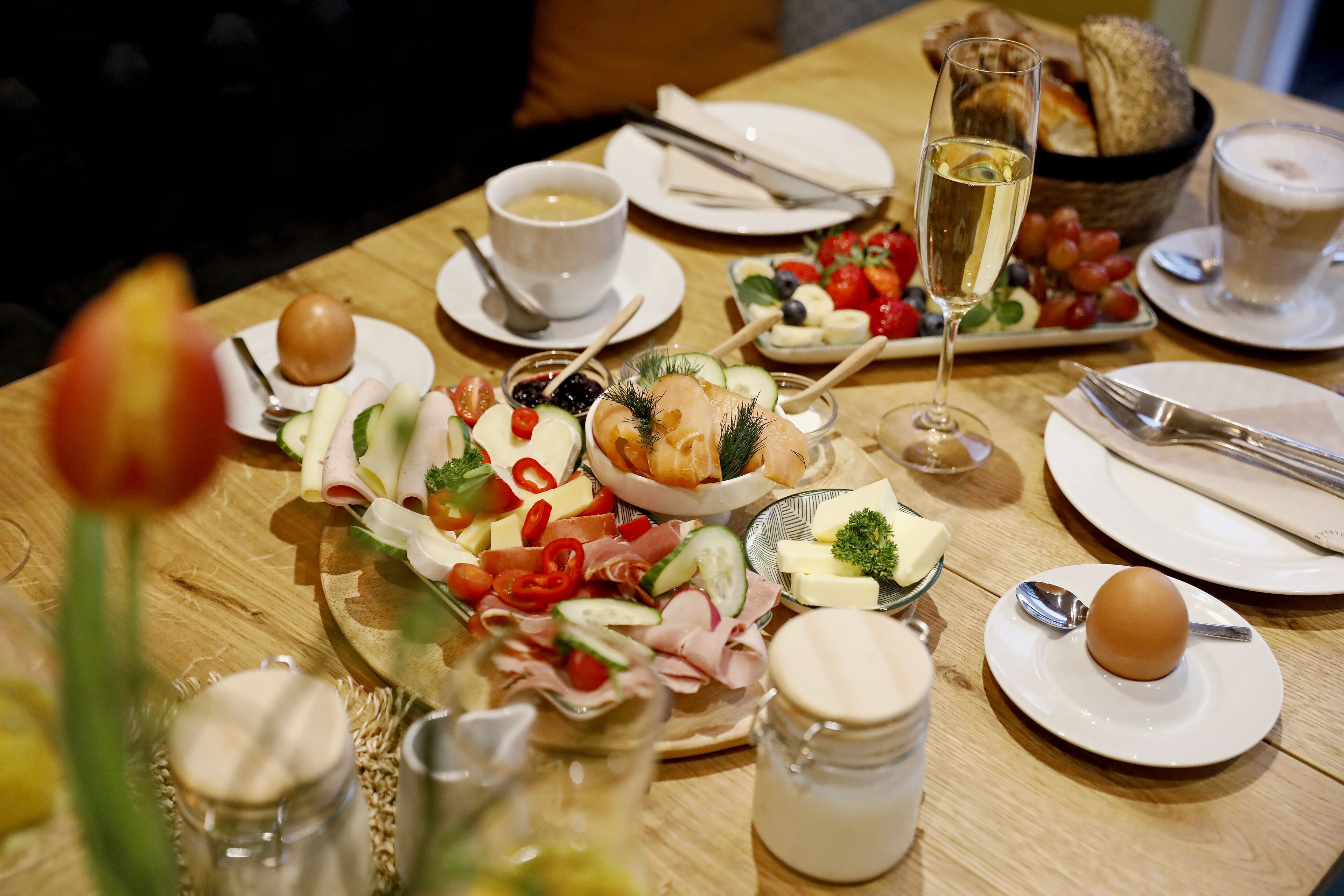 A table set for a meal with various dishes, including a glass of champagne, bread, and a selection of cheeses and meats.